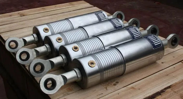 Four finished cylindrical hydraulic snubber units with spherical-eye connections on a wooden pallet
