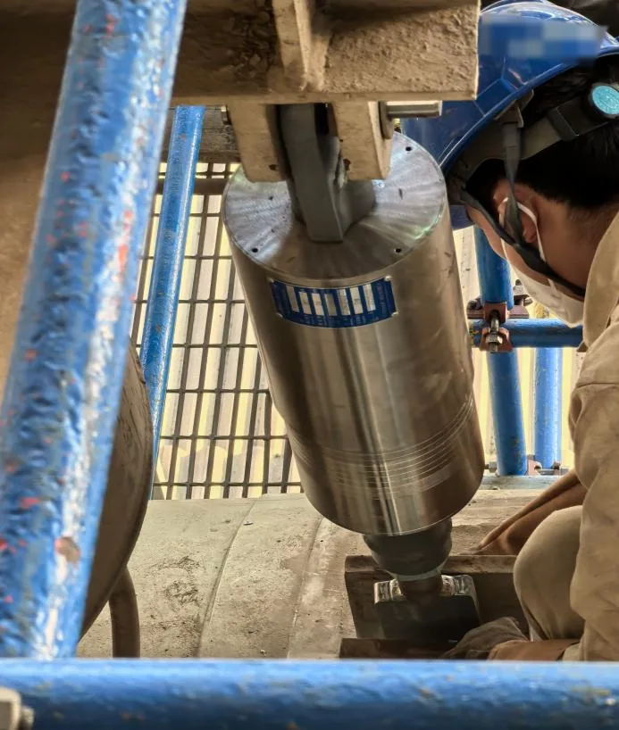Worker installing a cylindrical damping unit at an anonymized power facility, with helmet organization mark pixelated