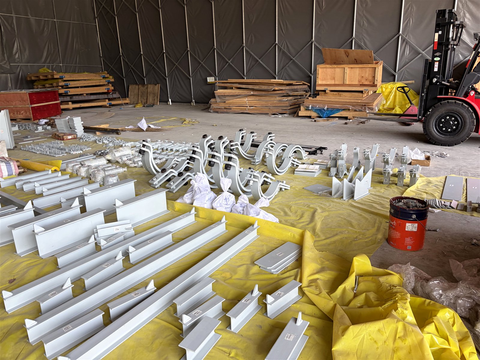 Painted pipe shoes, clamp bases and H-beam support assemblies staged on tarpaulin for dispatch