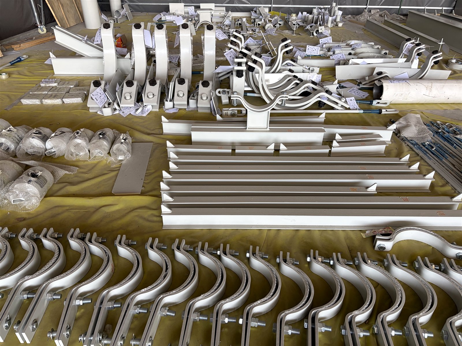 Pipe clamps, shoes and fabricated support assemblies arranged in rows inside the manufacturing base