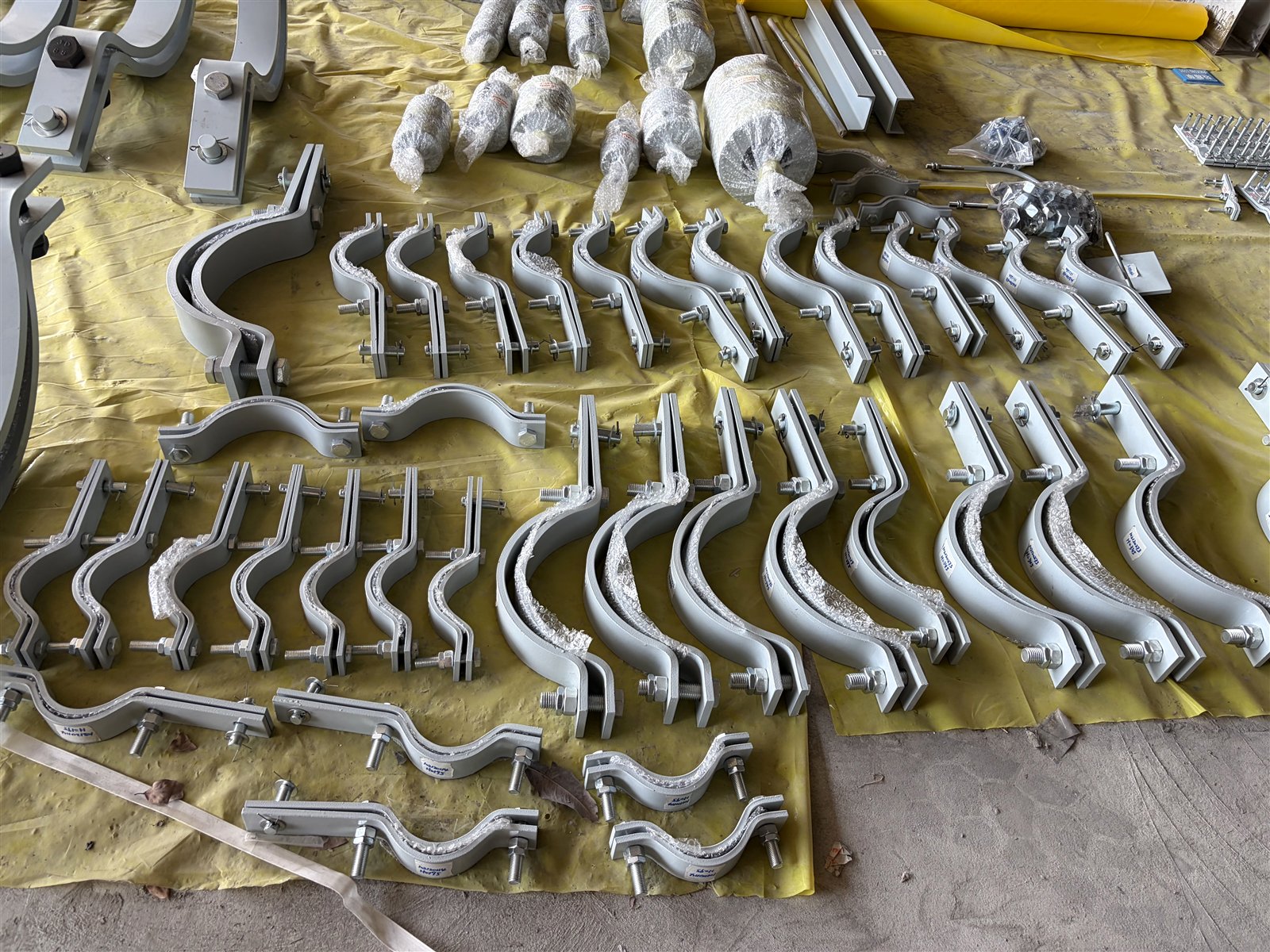 Rows of lined three-bolt pipe clamps with fasteners fitted, staged for a bulk order